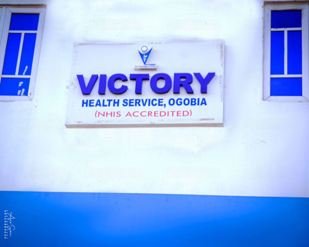 Victory Health Service, Ogobia – NHIS Accredited Facility - Victory College of Health Sciences and Technology Front view of Victory Health Service, Ogobia building sign showing NHIS accreditation, flanked by two blue window panels.