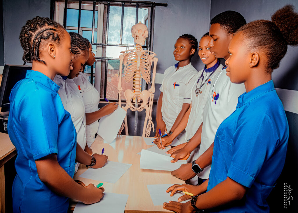 Anatomy Lab Session – Victory College Students in Practical Training - Victory College of Health Sciences and Technology Group of Victory College health science students in uniforms taking notes around a table with a human skeleton model during an anatomy class