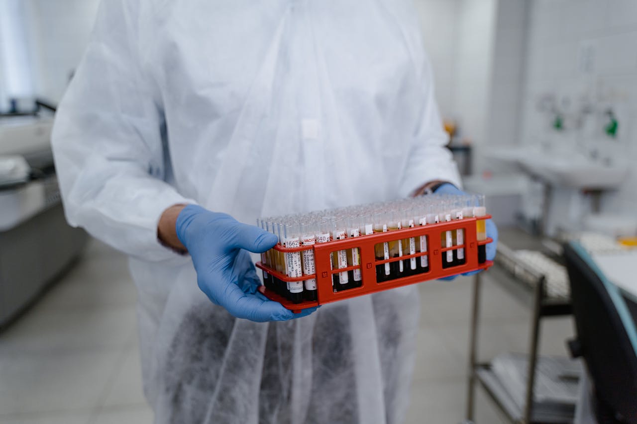 Scientist in protective gear holding a rack of test tubes in a laboratory setting, highlighting research work.